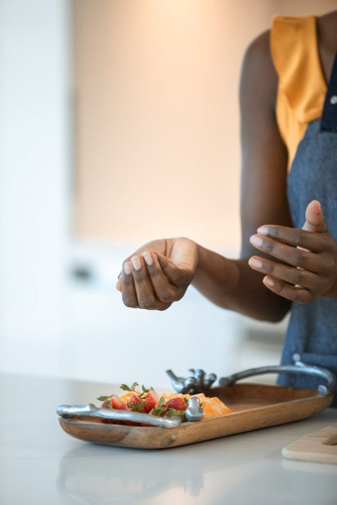 Close-up of hands preparing a fruit and cheese platter on a wooden tray.